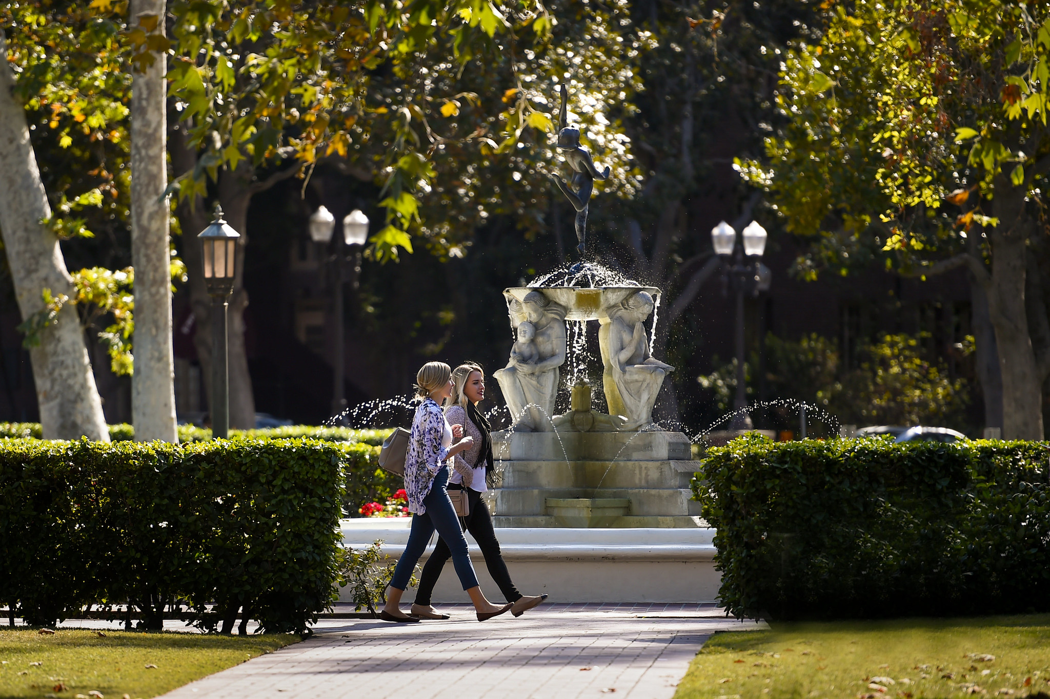 Two people walking past Alumni Park Fountain